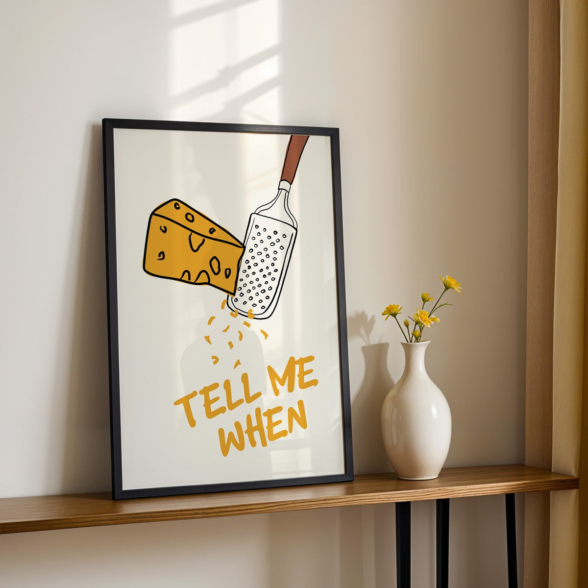 Tell me when cheese grater print in a black frame on a console table with daisies