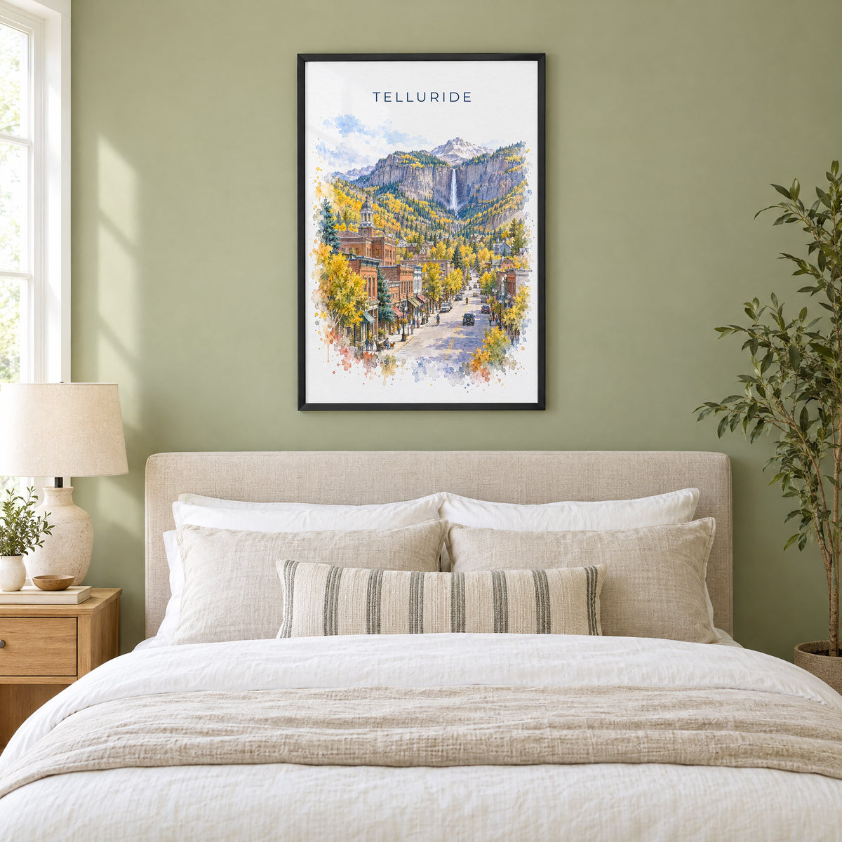 Telluride watercolor print in a black frame above an upholstered headboard in a sage green bedroom