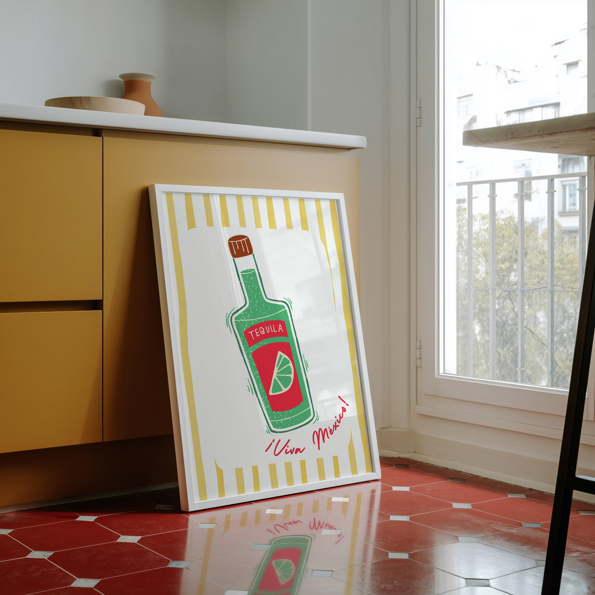 Tequila bottle print in a white frame against yellow cabinets on a red tiled floor