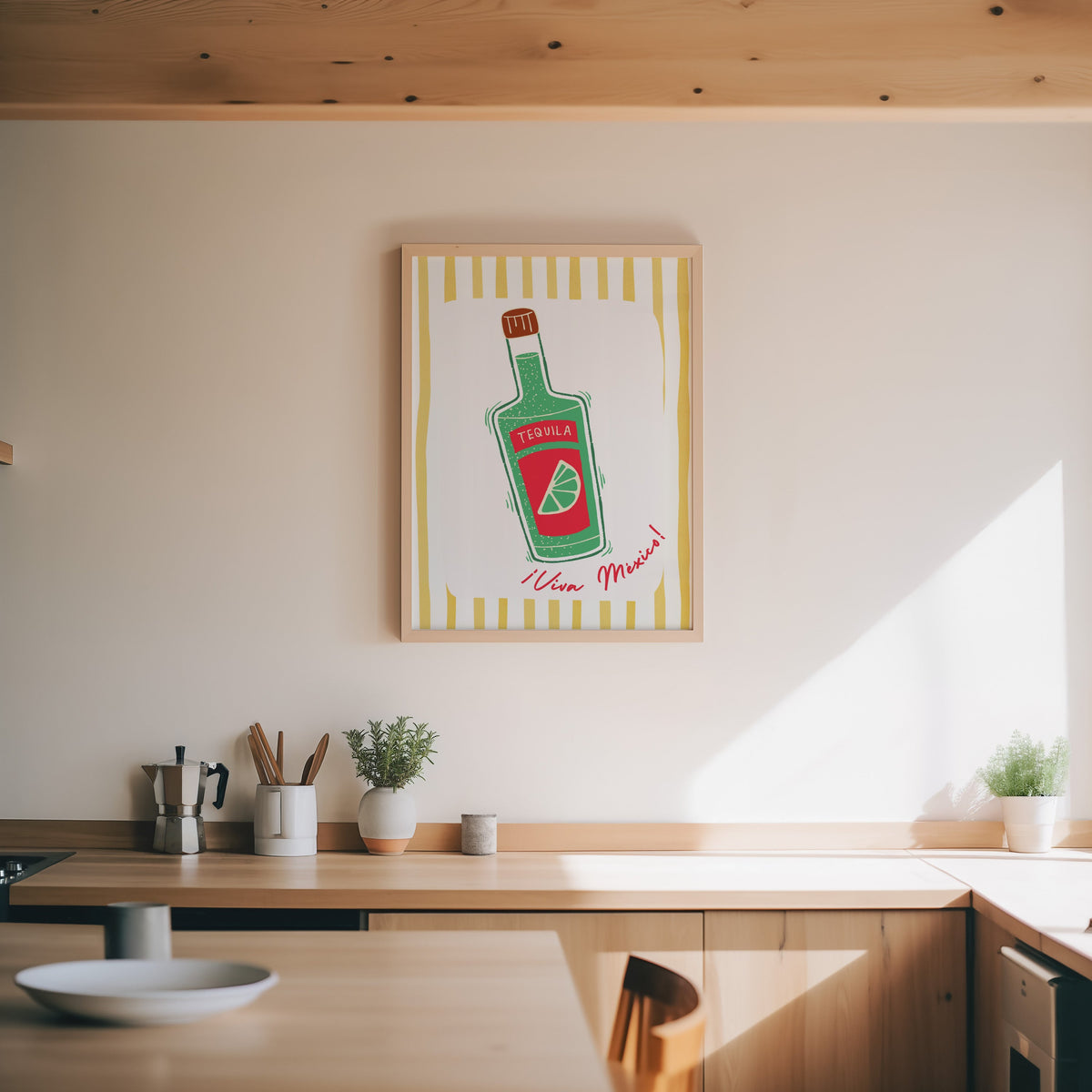 Tequila bottle print in an oak frame above a wood counter with a moka pot and herbs