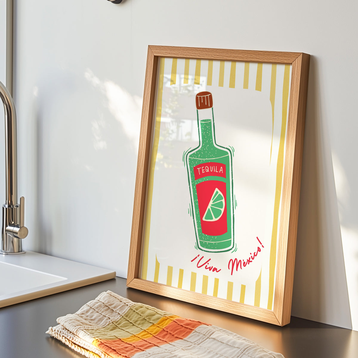 Tequila bottle print in an oak frame by the kitchen sink beside a striped tea towel