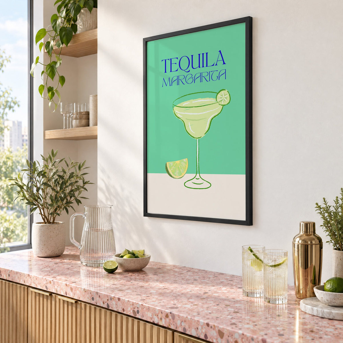 TEQUILA MARGARITA green glass and lime print in a black frame above a pink terrazzo cocktail counter with limes, seen at an angle