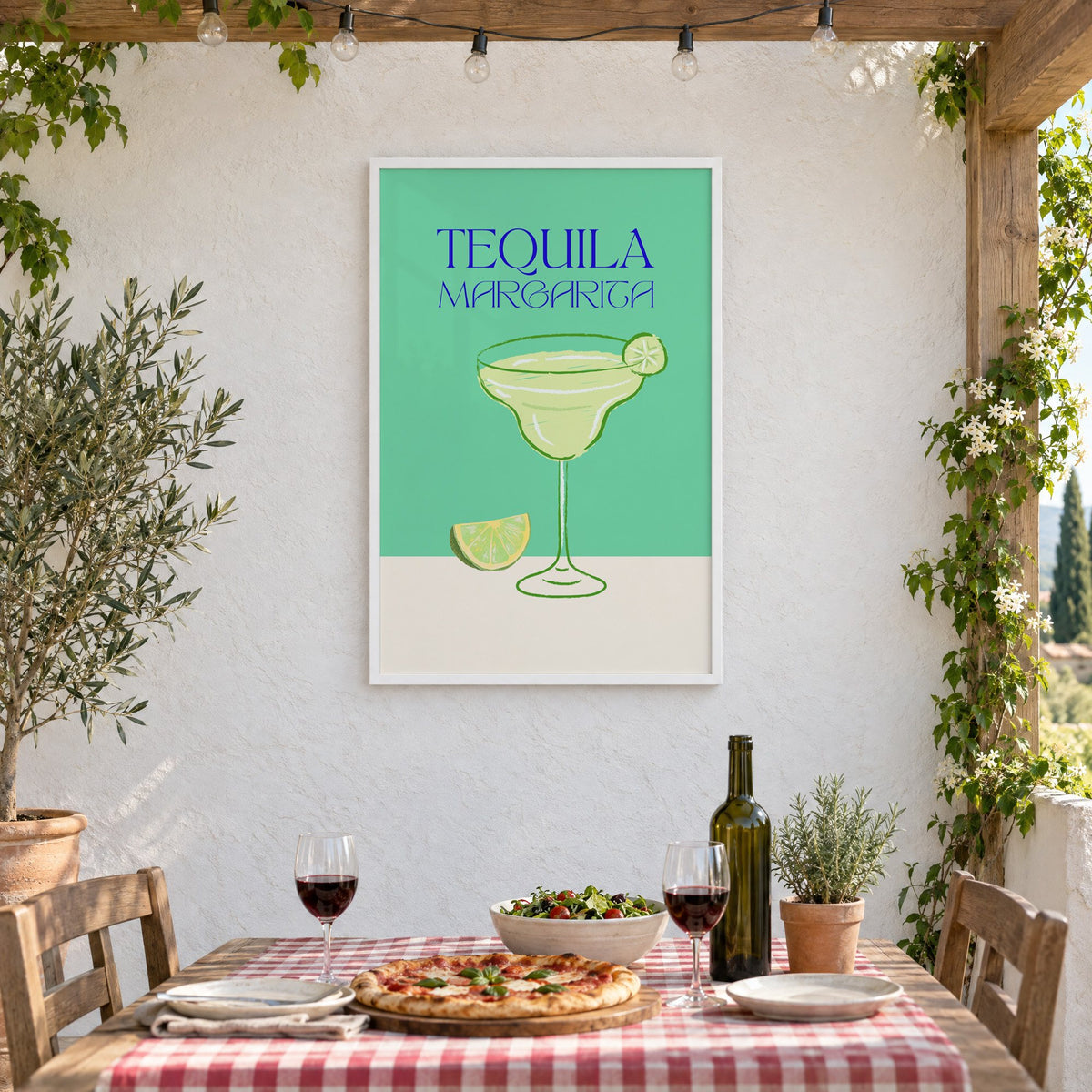 TEQUILA MARGARITA green glass and lime print in a white frame on a stucco wall above a checked-cloth table with pizza and red wine