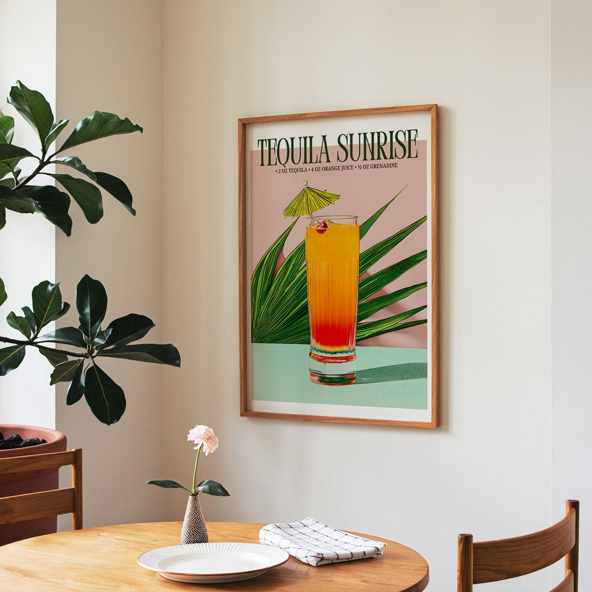 Tequila sunrise recipe print in a walnut frame above a round table beside a fiddle-leaf fig