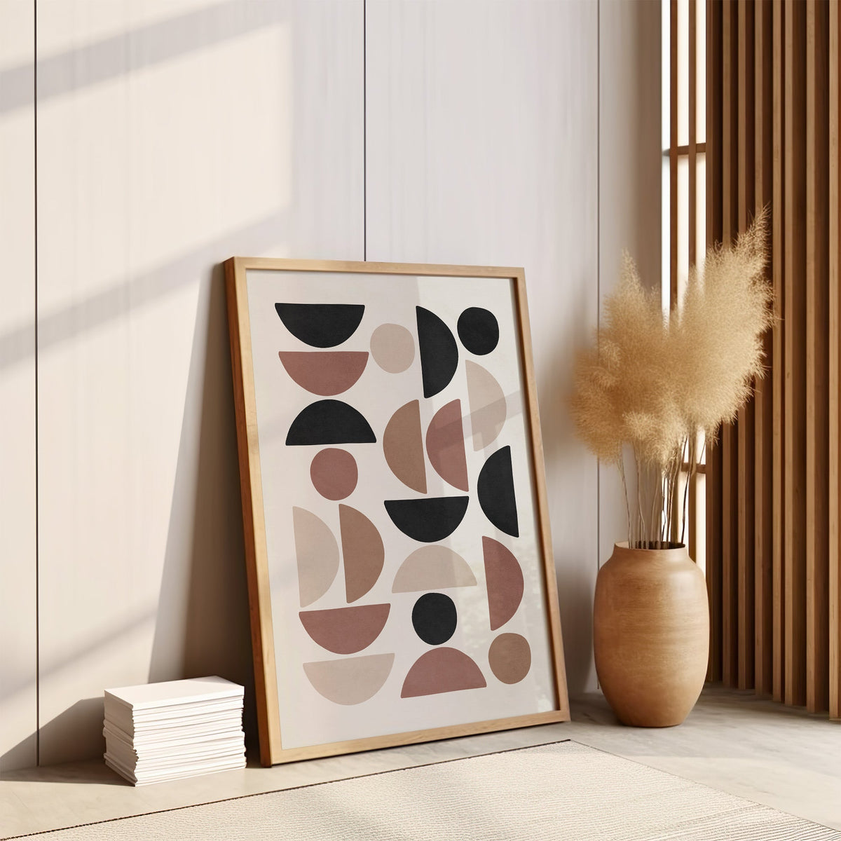 Terracotta and black half circle mosaic print in an oak frame leaning on the floor by pampas grass and a wood slat screen
