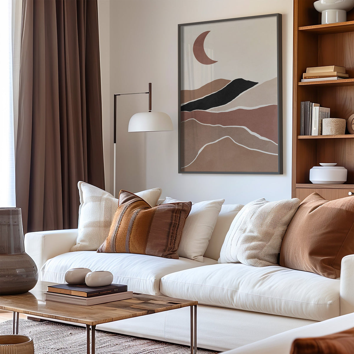 Terracotta crescent moon over hills boho print in a black frame above a cream sofa with brown striped pillows
