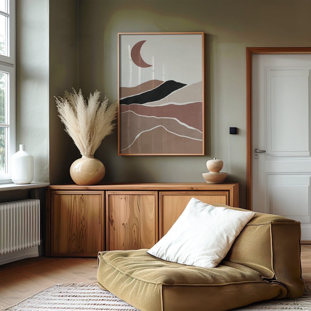 Terracotta crescent moon over hills boho print in an oak frame on an olive green wall above a wood sideboard with pampas
