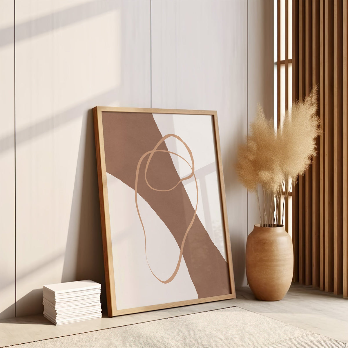 Terracotta diagonal band and loop line print in an oak frame leaning on the floor by pampas grass and a wood slat screen