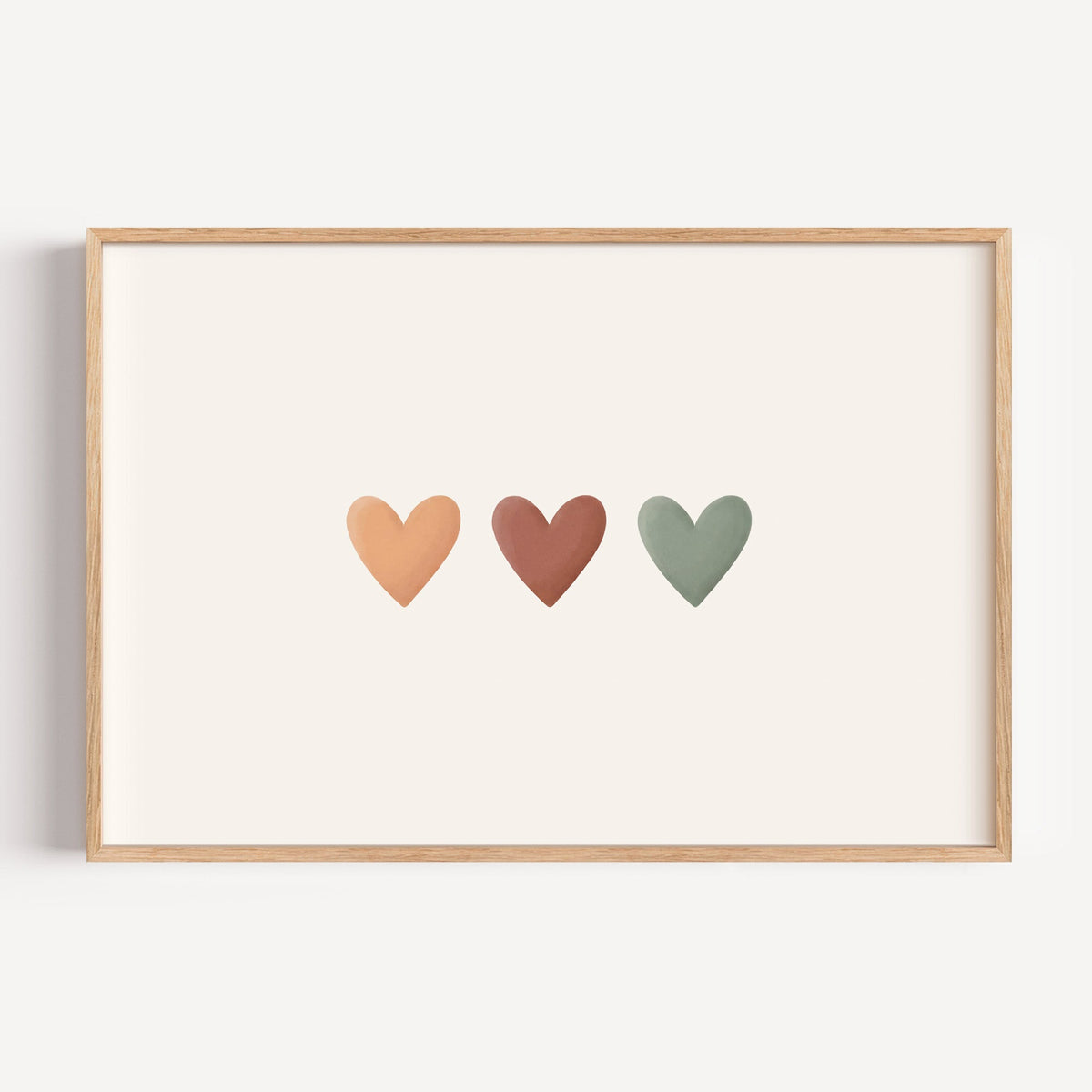 Three peach, terracotta and sage hearts in a row nursery print in a light oak frame on a plain white wall