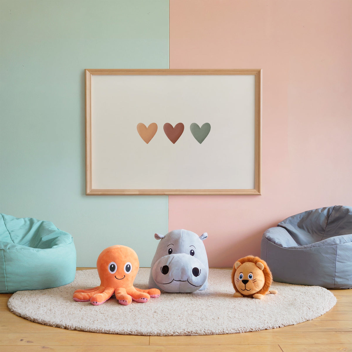 Three peach, terracotta and sage hearts in a row nursery print in an oak frame on a mint and pink wall above plush toys