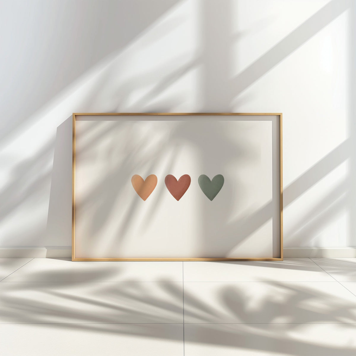 Three peach, terracotta and sage hearts in a row nursery print in a thin oak frame leaning on a tiled floor in dappled sunlight