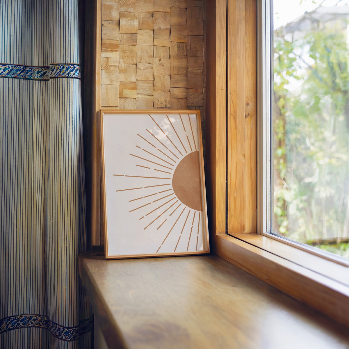 Terracotta half sun at right edge, dashed rays, boho print in a light wood frame leaning on a wooden window sill by a garden view