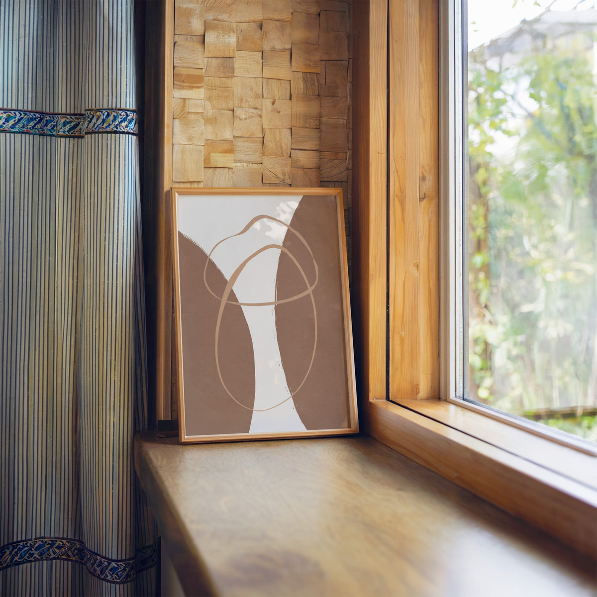 Terracotta twin arches and loops boho print in a light wood frame leaning on a wooden window sill by a garden view