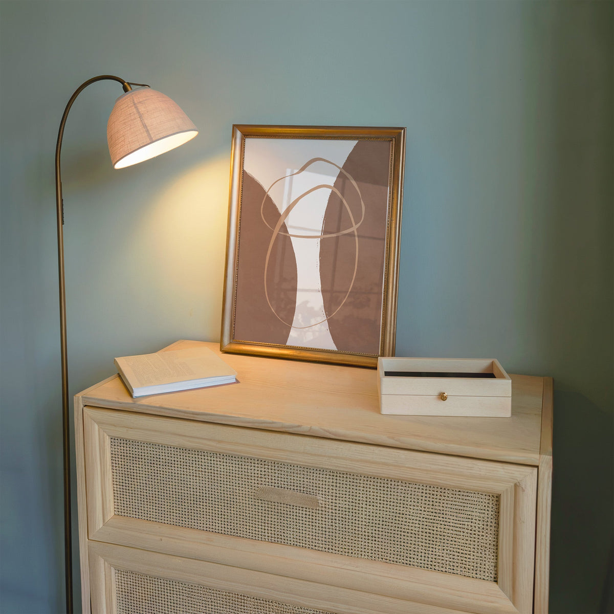 Terracotta twin arches and loops boho print shown in a gold frame on a cane dresser lit by a floor lamp