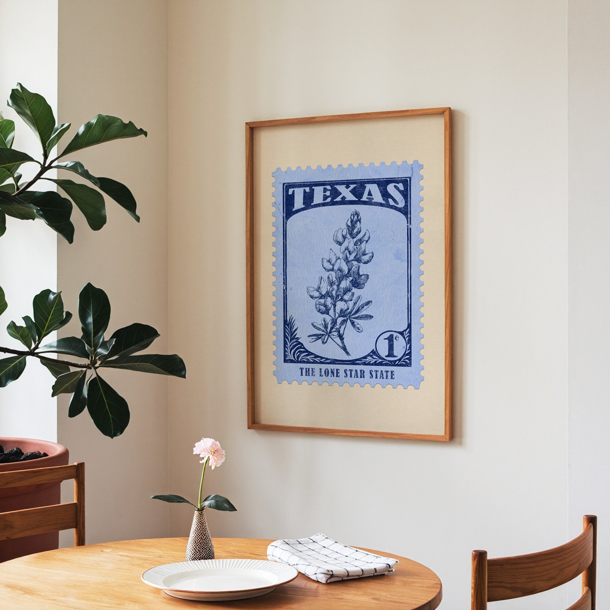 Texas state flower print framed above a round wooden table with a single bloom in a vase and books