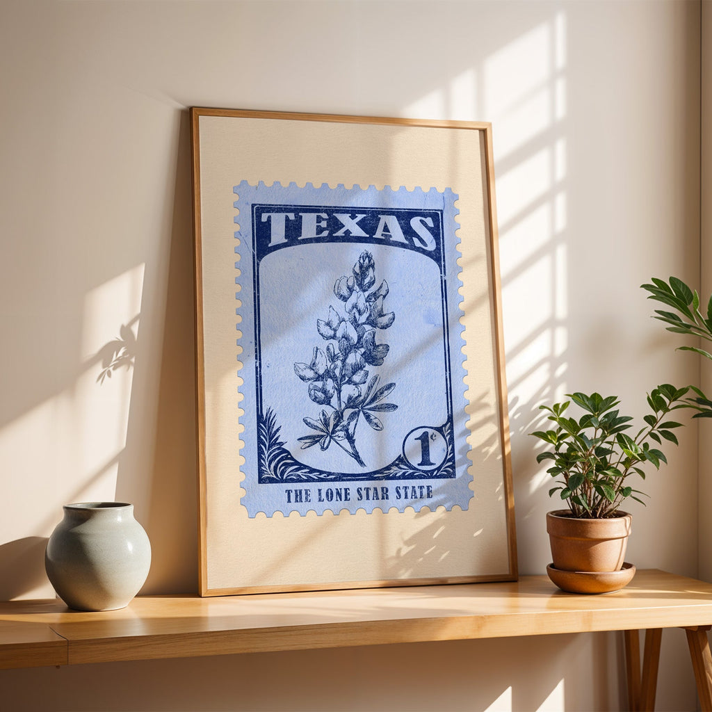Texas Bluebonnet stamp print in a light oak frame leaning on a wooden table beside a stoneware vase