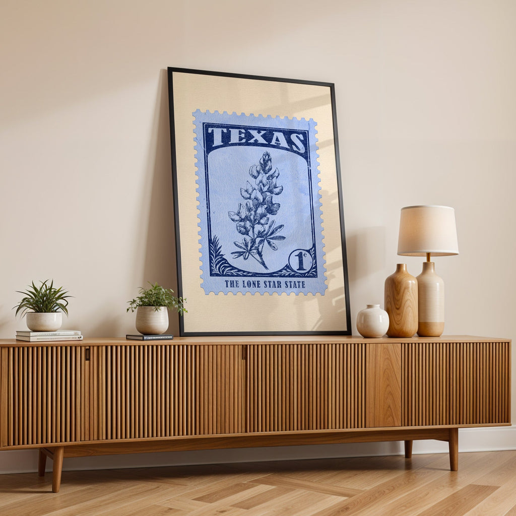 Texas state flower print in a black frame leaning on a fluted wood credenza with vases and a lamp