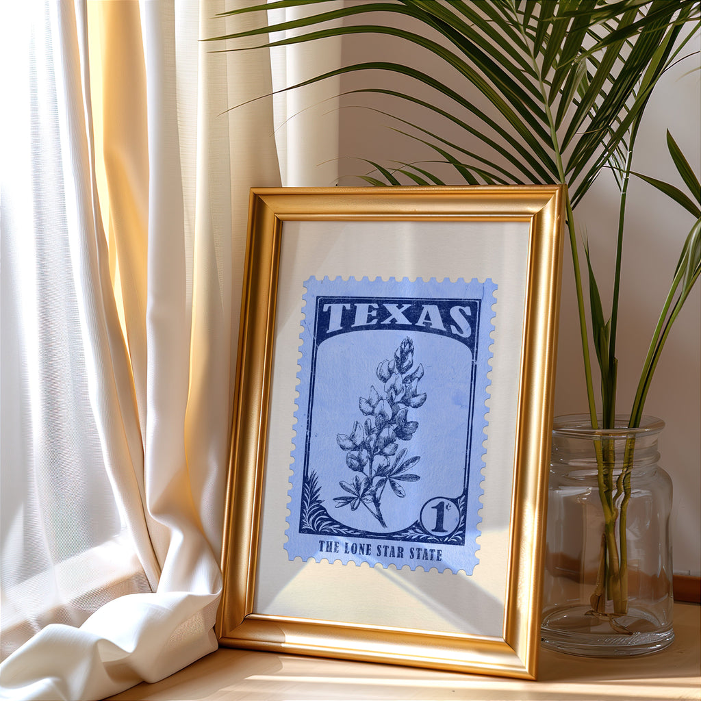 Texas stamp print in a gold frame leaning by a cream curtain with a palm in a glass jar