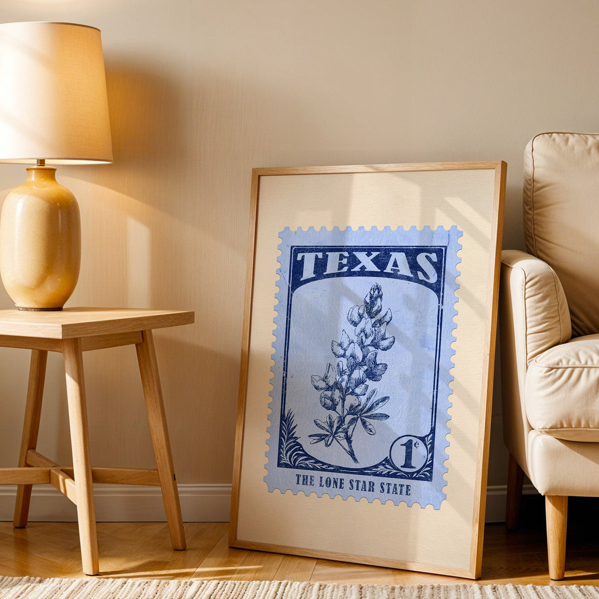 Texas stamp print in a wood frame resting on the floor beside a beige armchair and a yellow lamp
