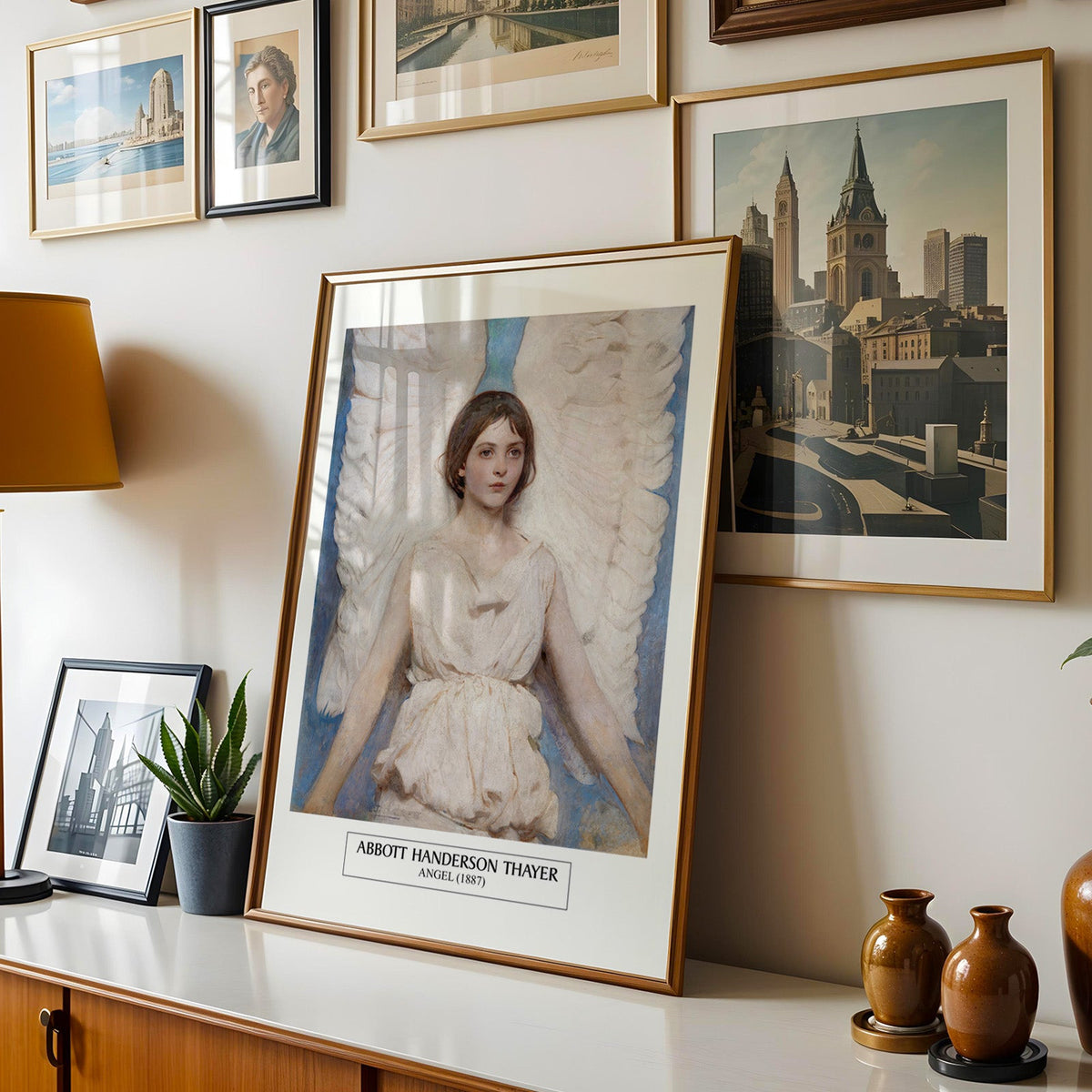 Angel print shown in a gold frame leaning on a sideboard in a gallery wall