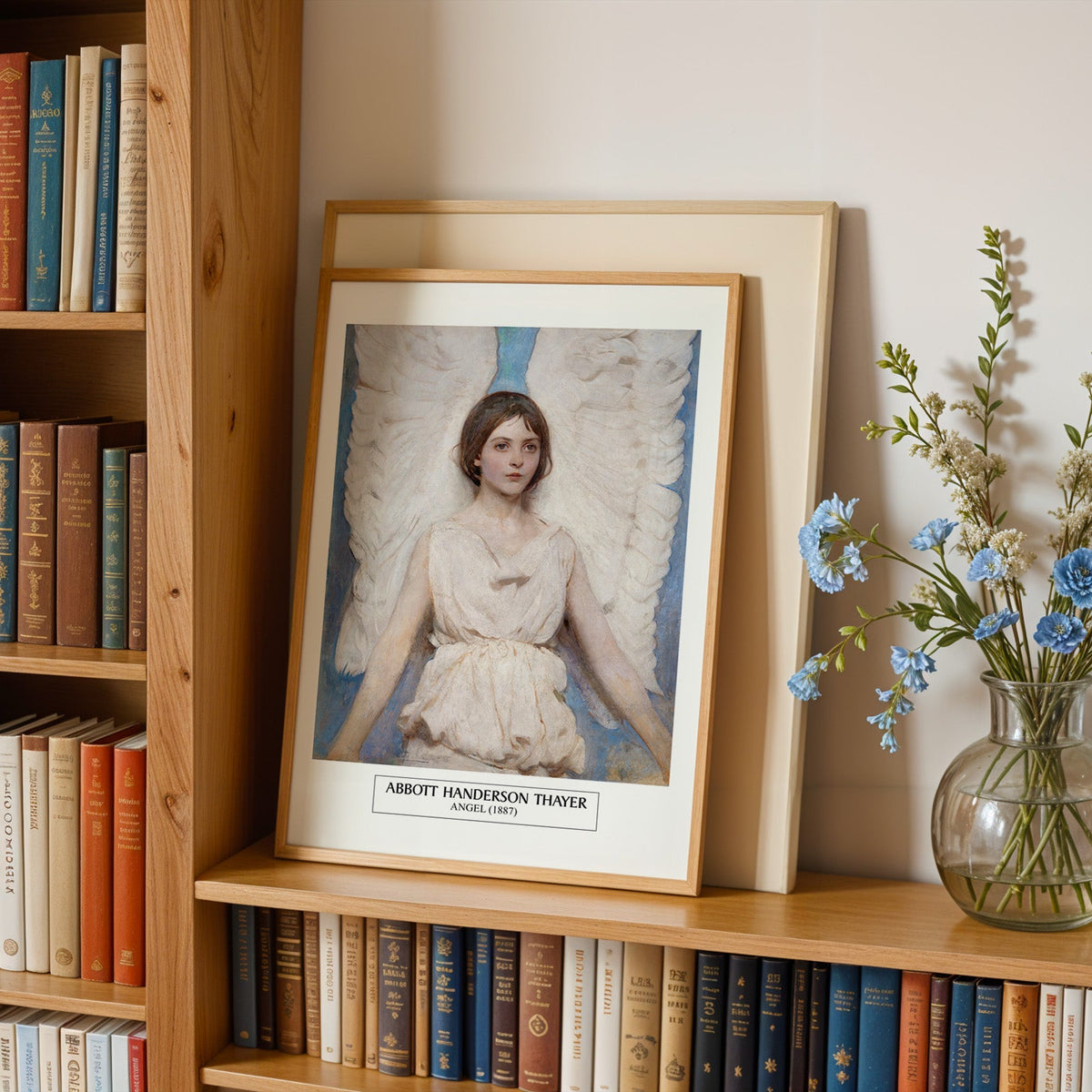 Thayer angel print in an oak frame leaning on a bookshelf beside blue flowers