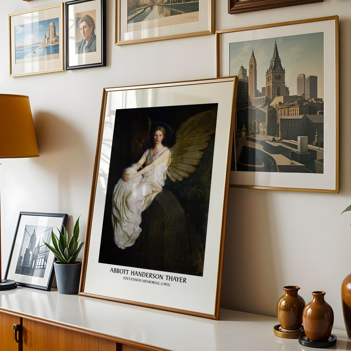 Angel print shown in a gold frame leaning on a sideboard in a gallery wall
