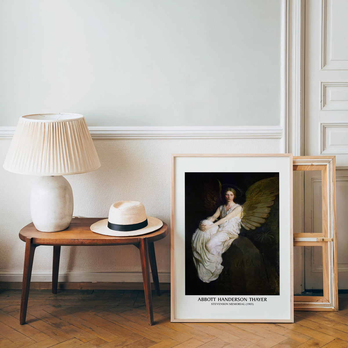 Angel poster in a light wood frame leaning by a bench and panama hat