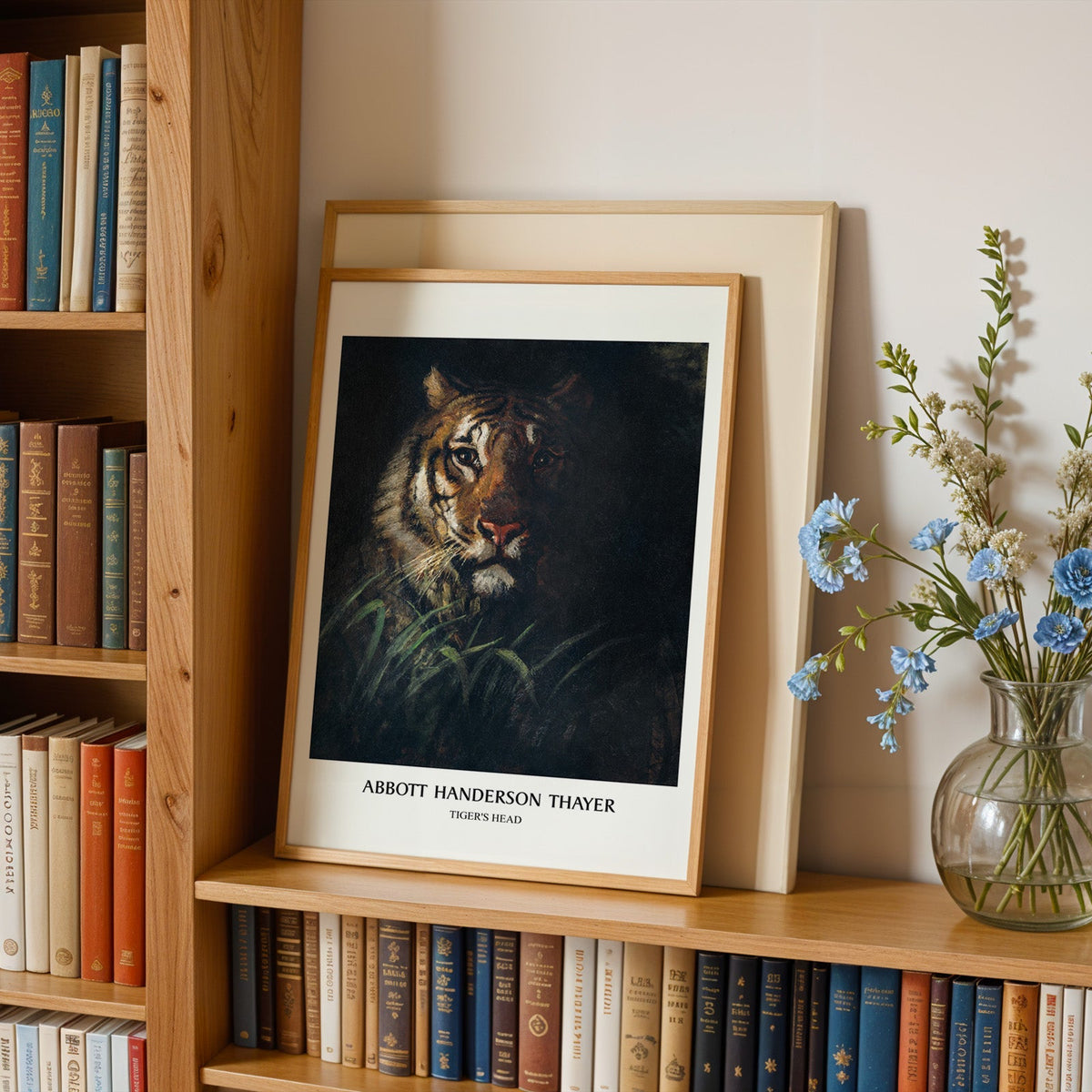 Tiger's Head print in an oak frame leaning on a bookshelf beside blue flowers