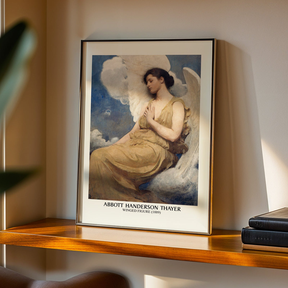 Winged Figure print in a black frame on a walnut shelf in warm evening light