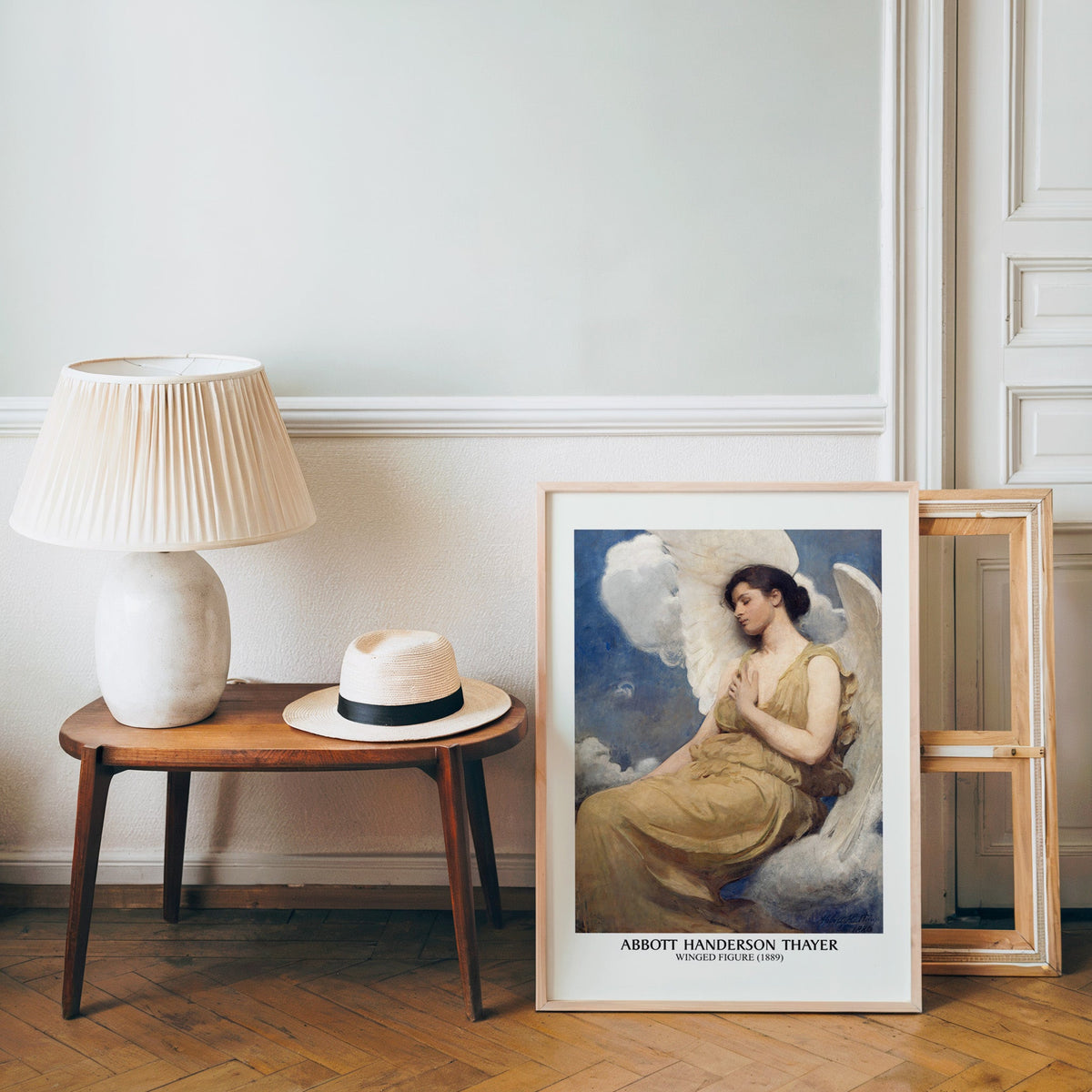 Thayer angel poster in a light wood frame leaning by a bench and panama hat