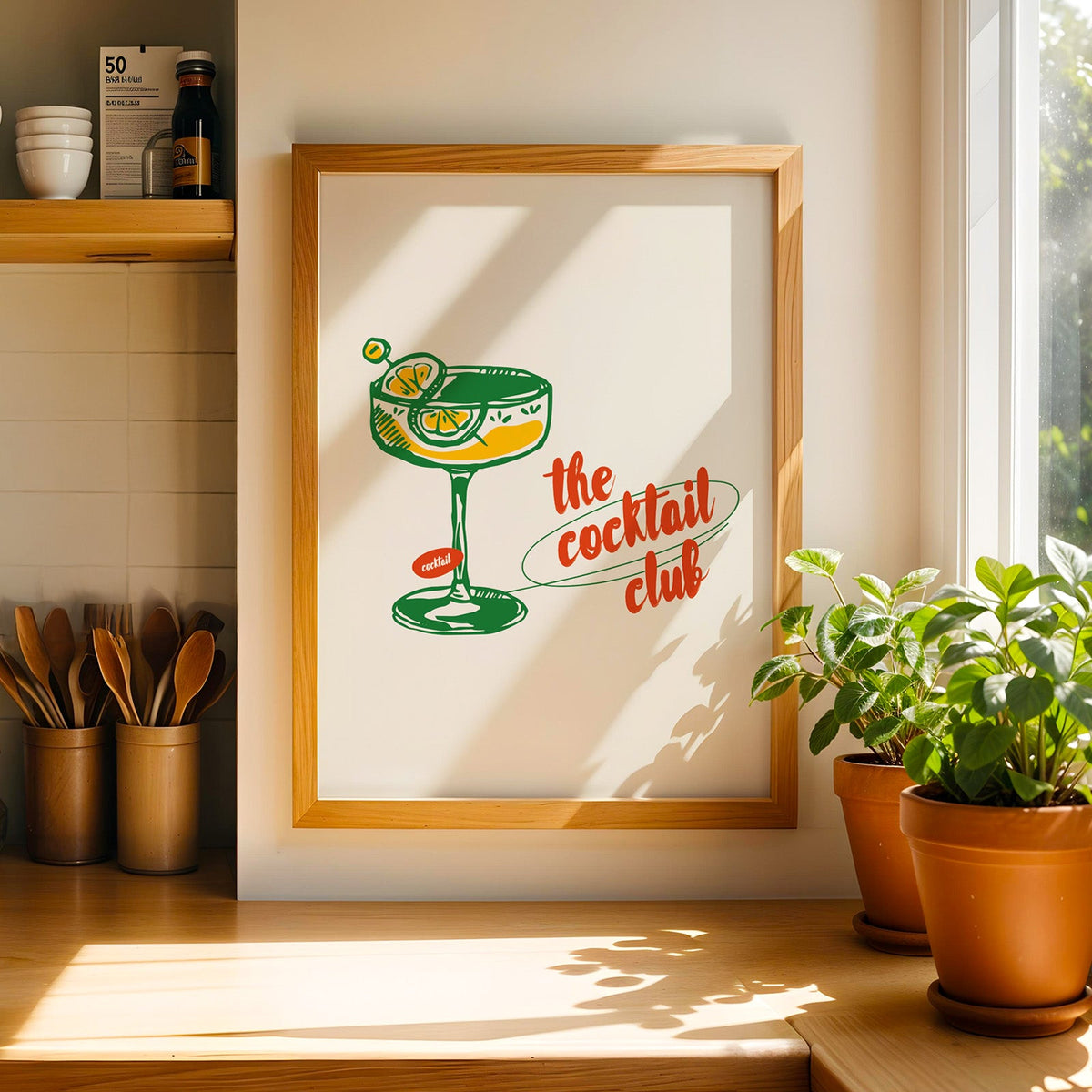 Coupe glass bar cart print in a light wood frame on a butcher block counter by crocks of wooden utensils