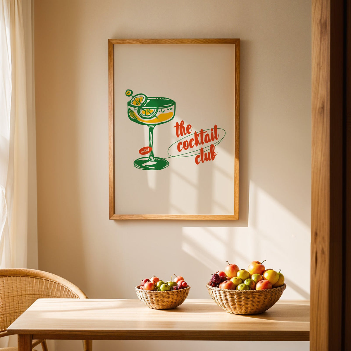 Green coupe glass print in an oak frame hung above a dining table with wicker bowls of fruit