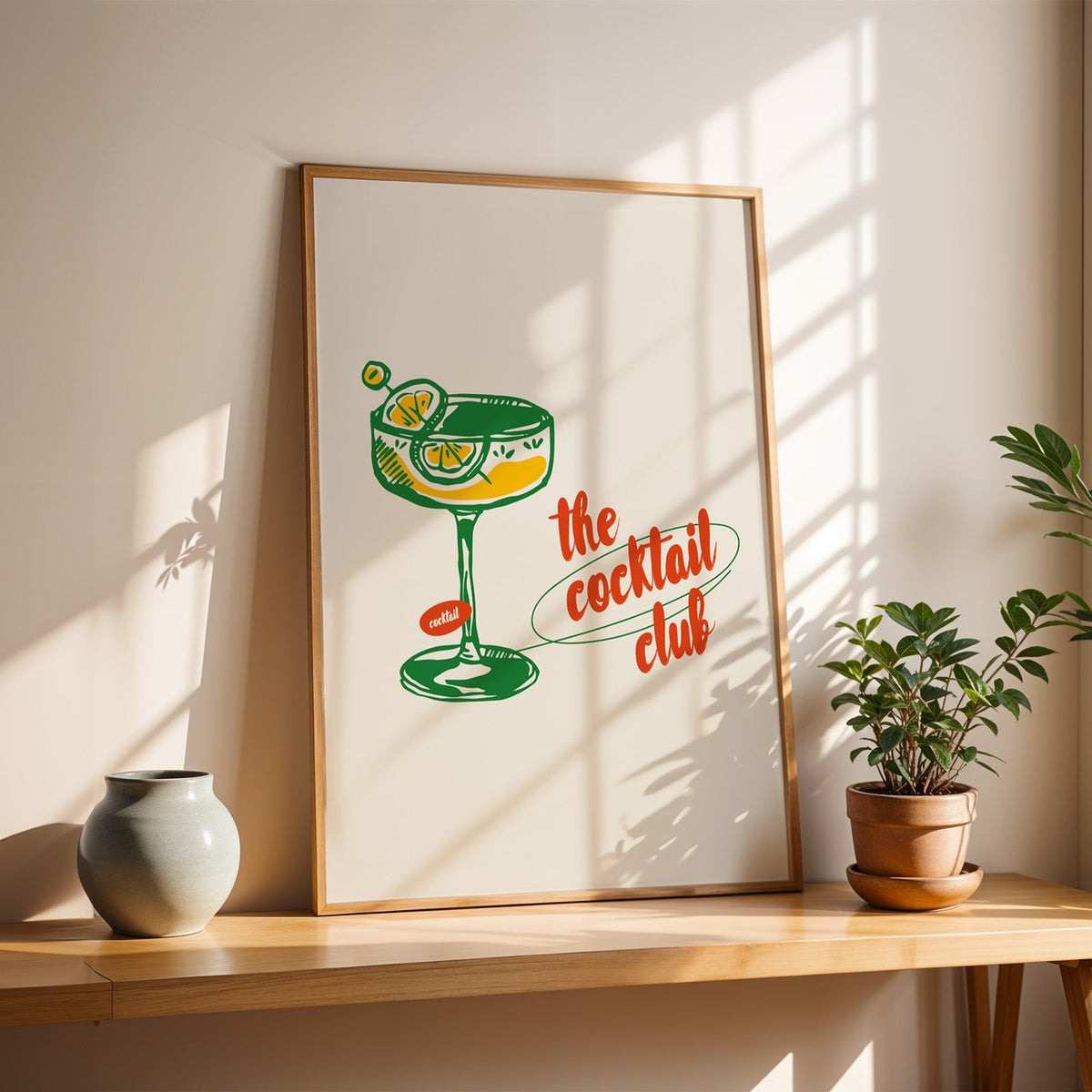 The Cocktail Club poster in a slim oak frame on a sunlit wood console with a stoneware vase