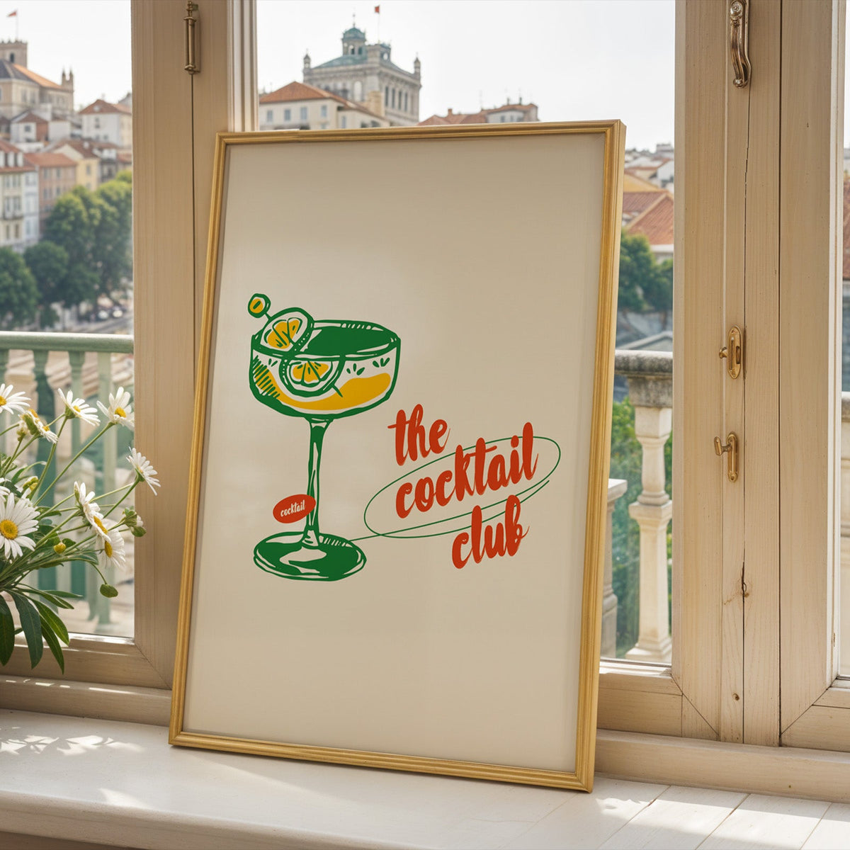 Cocktail club print in a gold frame on a window sill overlooking a hillside town
