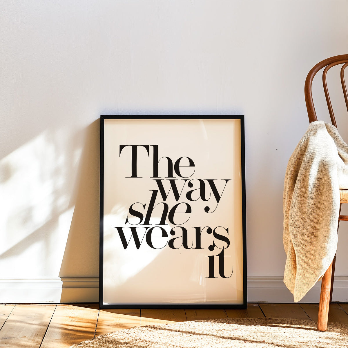 The way she wears it serif lettering print in a black frame leaning on a wood floor beside a bentwood chair