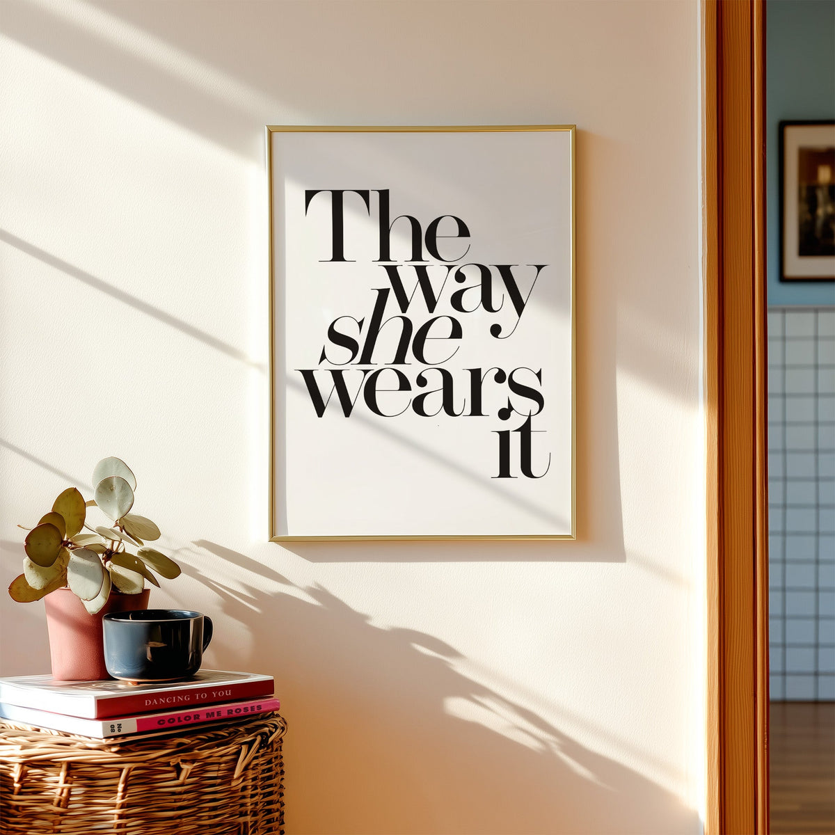 The way she wears it serif lettering print shown in a gold frame above a wicker basket and stacked books