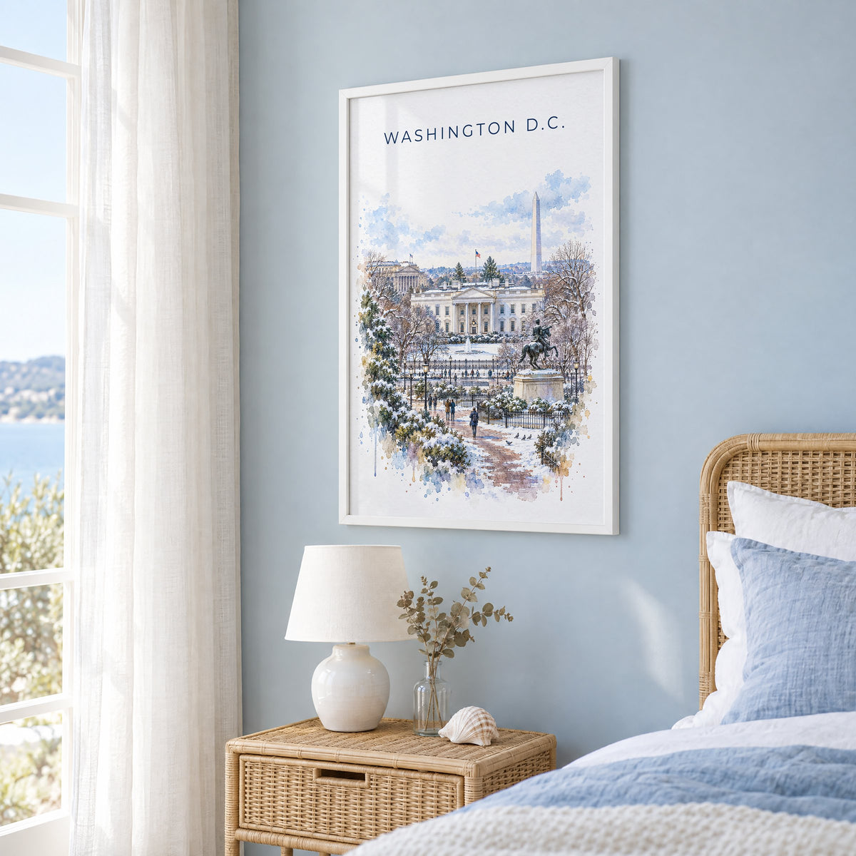 White House watercolor print in a white frame on a pale blue wall beside a rattan bed in a coastal bedroom