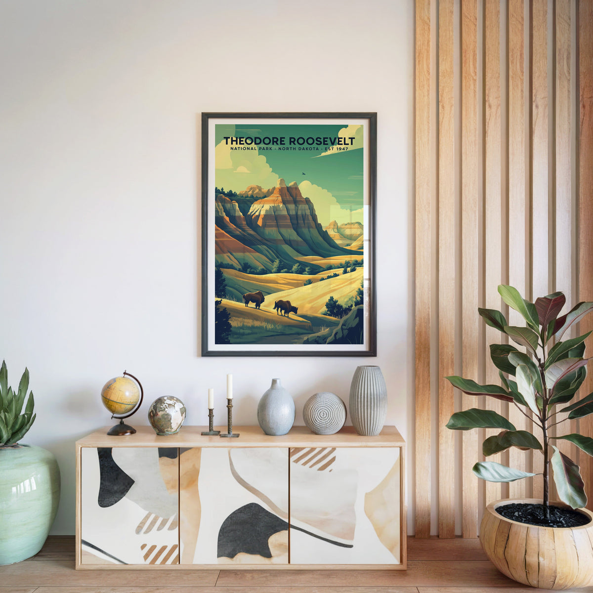 Theodore Roosevelt National Park print in a black frame above a light wood sideboard with a globe and vases