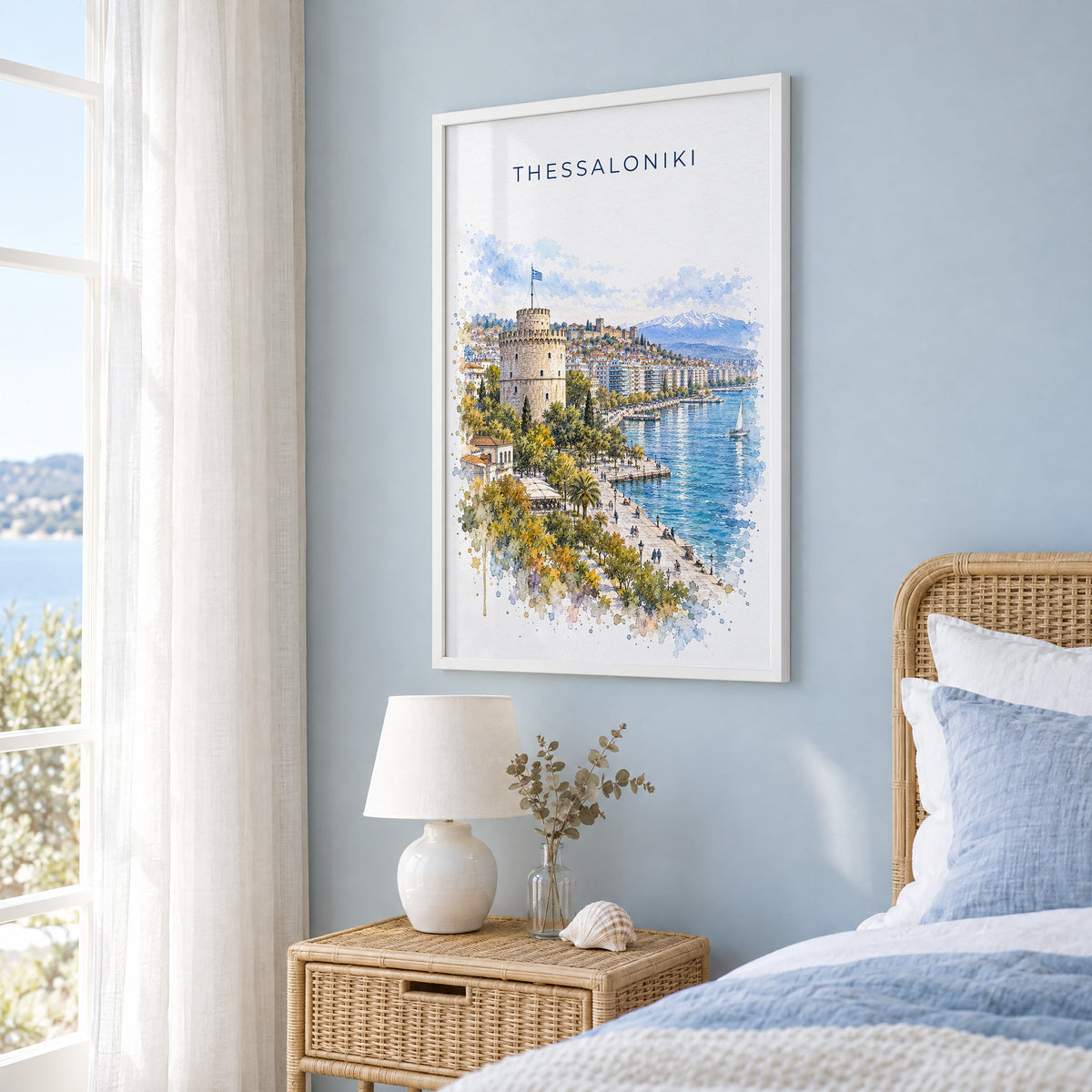 Thessaloniki watercolor print in a white frame on a pale blue wall beside a rattan bed in a coastal bedroom