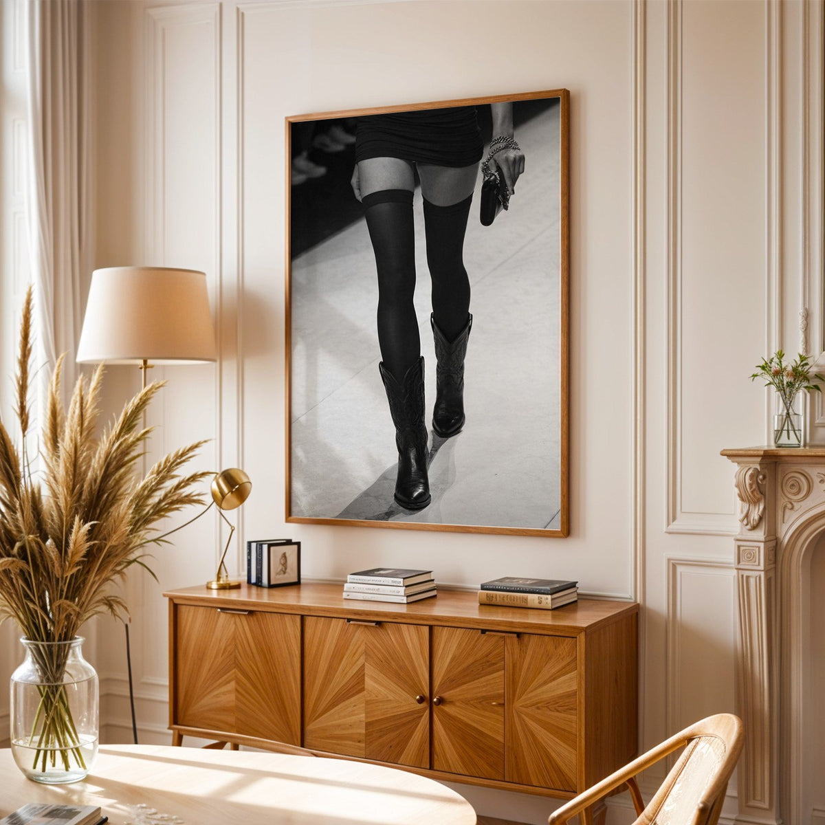 Legs in stockings and cowboy boots on runway print in an oak frame above a sunburst wood sideboard with pampas grass