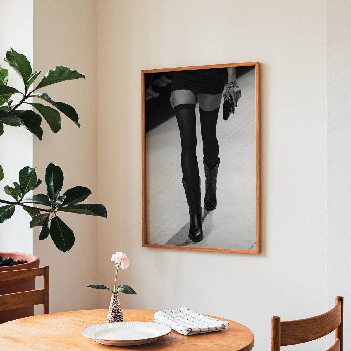 Legs in stockings and cowboy boots on runway print in a teak frame above a round wooden dining table
