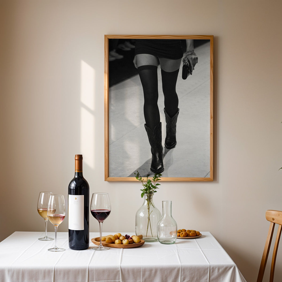 Legs in stockings and cowboy boots on runway print in an oak frame above a table set with red wine and glasses