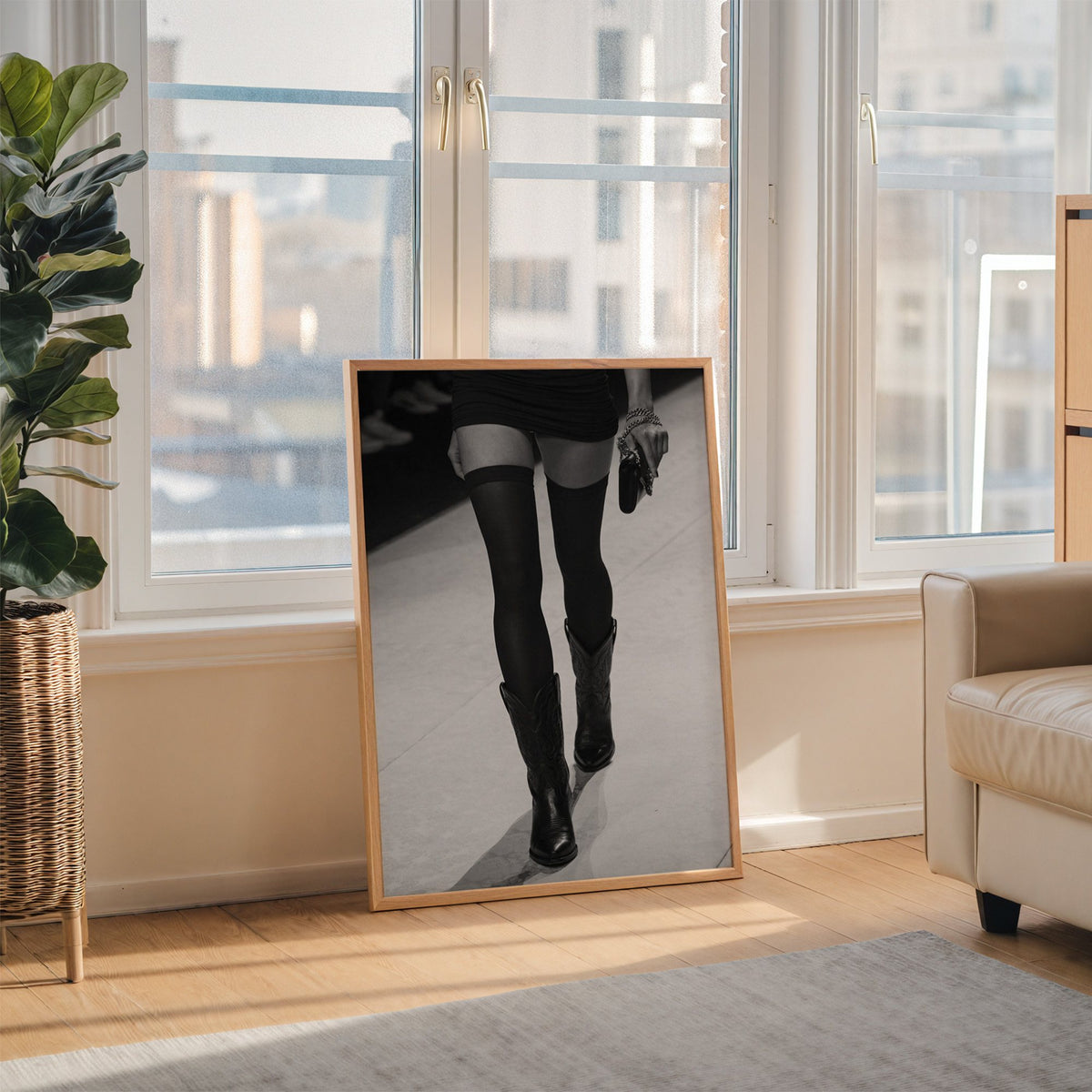 Legs in stockings and cowboy boots on runway print in an oak frame leaning on the floor beside a fiddle leaf fig