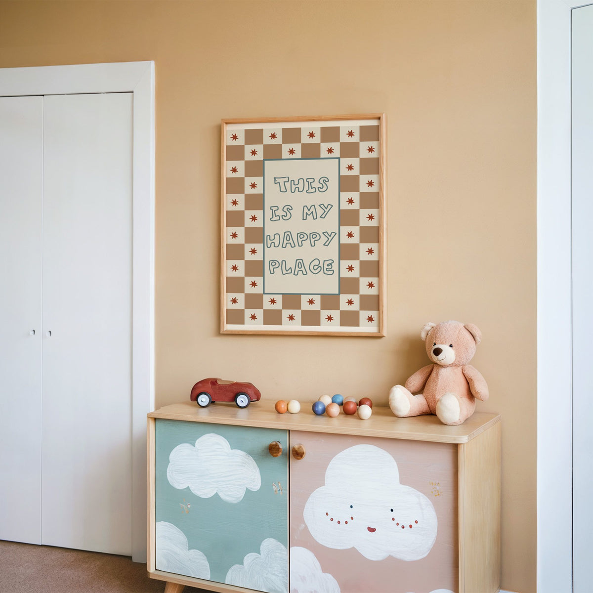 This is my happy place nursery print in an oak frame on a peach wall above a cloud-painted cabinet