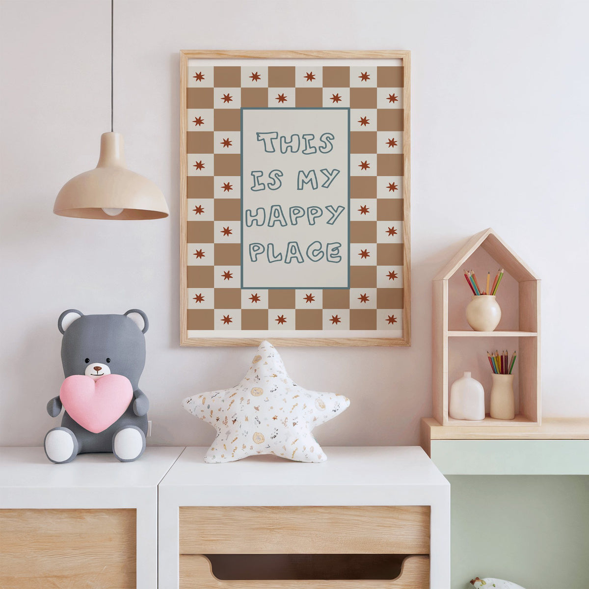 This is my happy place nursery print in an oak frame above a white dresser with a star pillow and house shelf
