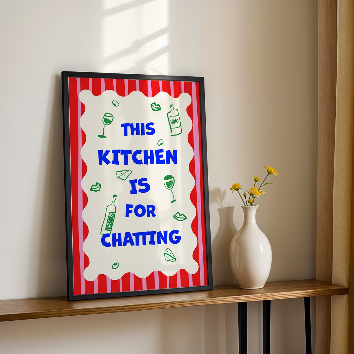 This kitchen is for chatting print in a black frame on a console table with daisies