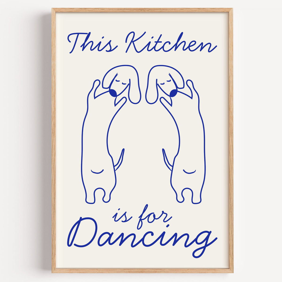 Dachshunds kitchen dancing print in a light oak frame on a plain white wall