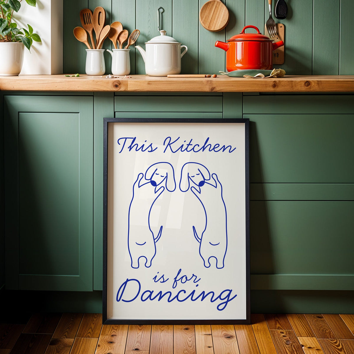 Dachshunds kitchen dancing print in a black frame against sage green cabinets