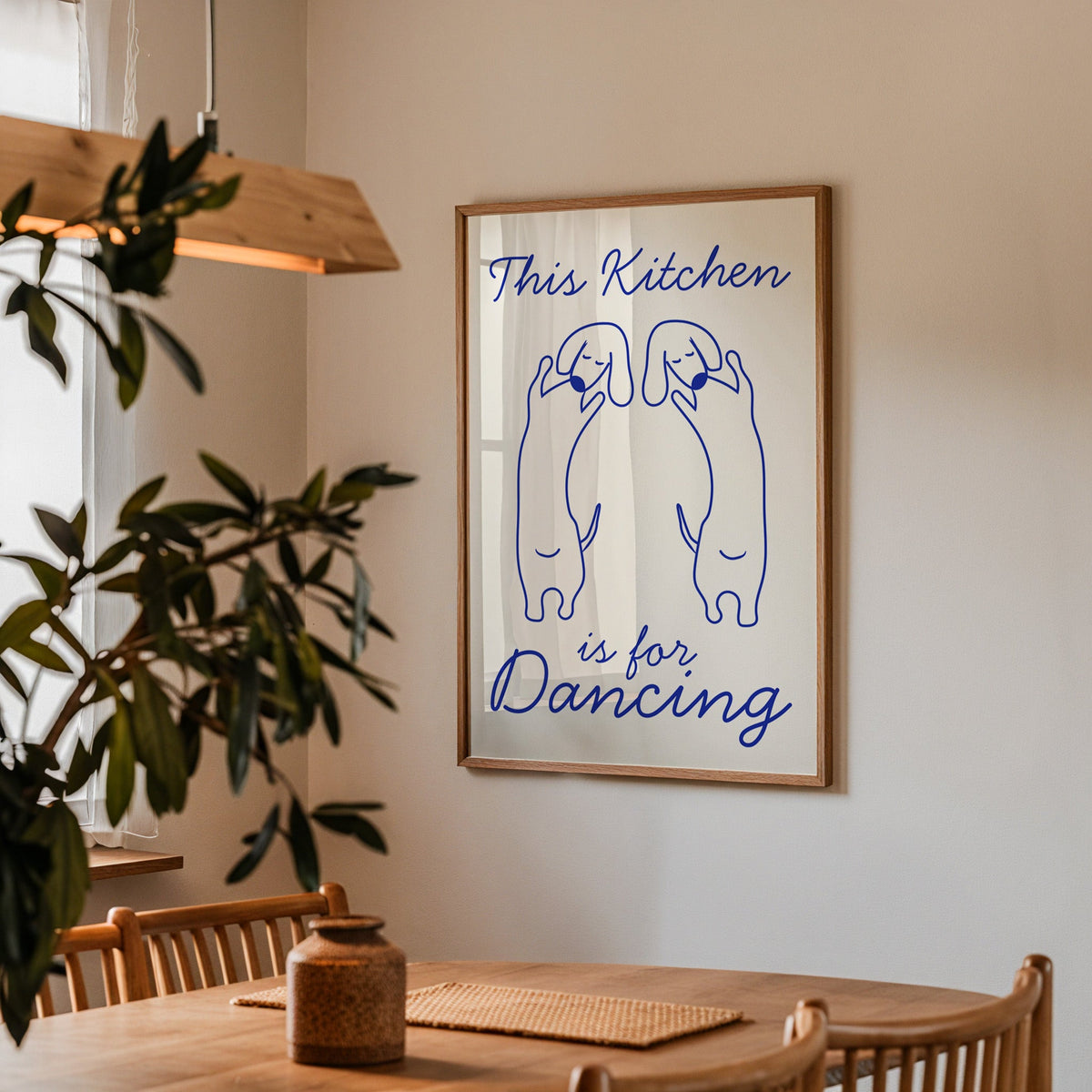 Dachshunds kitchen dancing print in a walnut frame above a table beside an olive tree