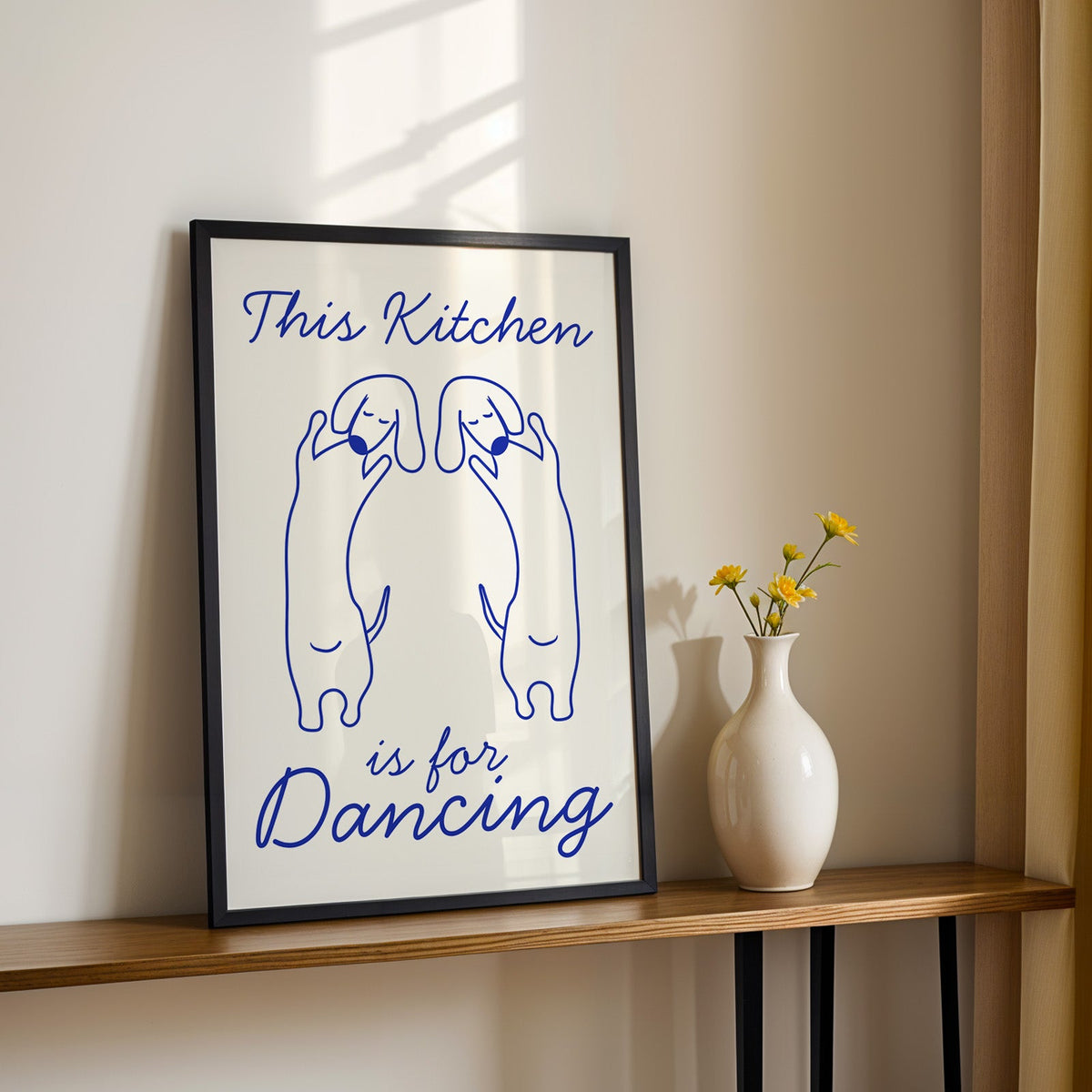 Dachshunds kitchen dancing print in a black frame on a console table with daisies